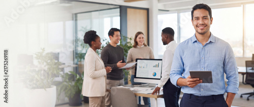 Businessman holding tablet with team in office stands smiling while diverse colleagues analyze data on computer screen in modern bright workspace for corporate business banner