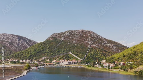 Panoramic view of Ston, Croatia, featuring historic fortress walls, Drums Tower, rugged mountains, traditional red-roofed houses, and the scenic Adriatic coast