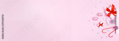 Minimal Christmas banner with white paper gift bag, presents, baubles and candy canes on soft pink copy space for holiday sales, social media ads and festive designs, flat lay.