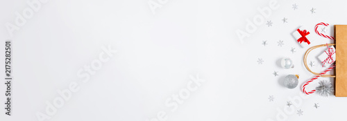 Holiday gift bag with tiny presents, candy canes and silver festive ornaments on white background with wide copy space for Christmas ads, seasonal banners and marketing layouts. Flat lay.