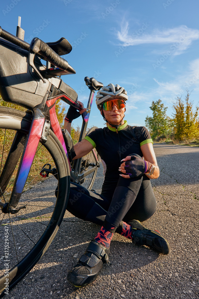 Fototapeta premium Female Cyclist Resting With Road Bike On Country Road During Sunny Outdoor Training Ride