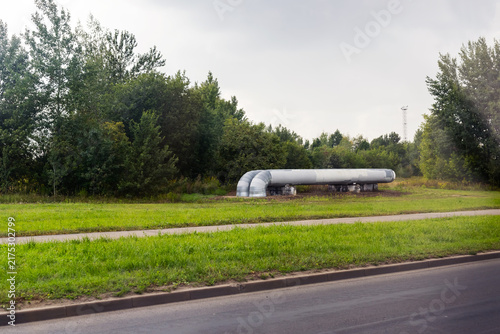 Obraz na plátne Long industrial pipeline aboveground crossing grassy roadside under cloudy sky w