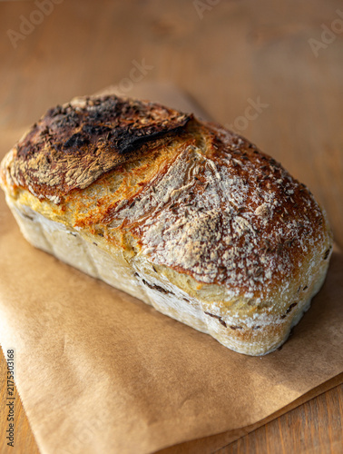 Freshly baked artisanal sourdough bread loaf sprinkled with caraway seeds, resting on baking paper over a wooden background, rustic bakery style.