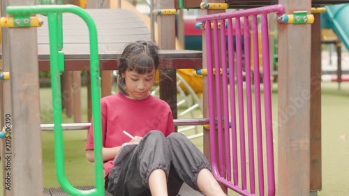 Asian kid enjoying a relaxing hobby, drawing digital art on tablet at outdoor school playground. Selective focus highlights creative elementary student spending personal leisure time with technology.