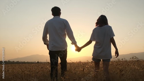 young boy and girl walking hand in hand through ripe wheat toward the sunset, young love and partnership, sharing happiness and life together, mutual trust, hope and emotional connection