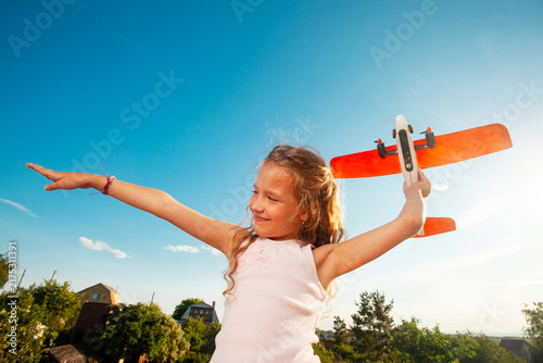 Fotografie Happy girl playing with toy airplane under blue sky