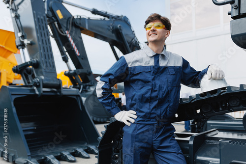 Foto Happy Caucasian young male driver of crawler excavator with hard hat standing by