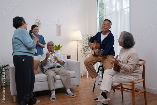 A group of elderly people are preparing for an activity: a senior woman holds a microphone and sings, and her friend plays guitar, enjoying music therapy at the nursing home.