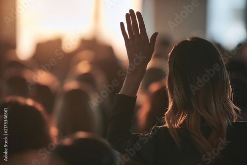 Woman raising her hand to ask a question during a seminar in a crowded conference room setting