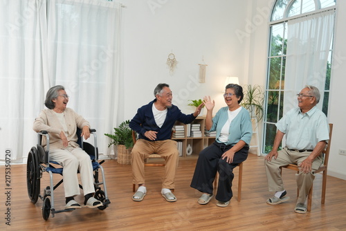 A group of elderly people are preparing to exercise, and an elderly woman in a wheelchair is in class while waiting for the group of senior citizens to sit and chat together at the nursing home.
