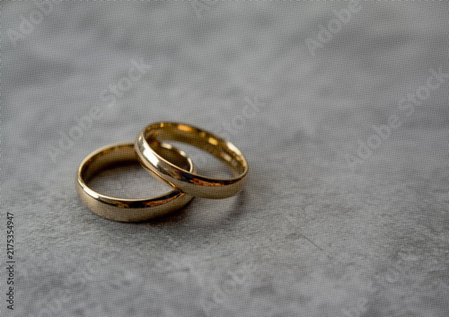 Fotografía Two interlocking gold wedding rings resting on a textured grey stone surface clo