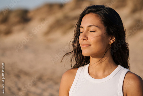 Serene Young Woman Meditating with Eyes Closed on Beach in Warm Sunset Golden Light