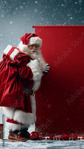 Santa stands beside a blank red panel. Snow gently falls around him in a quiet, magical setting. He holds a gift and smiles warmly. Perfect for holiday campaigns or Christmas messaging