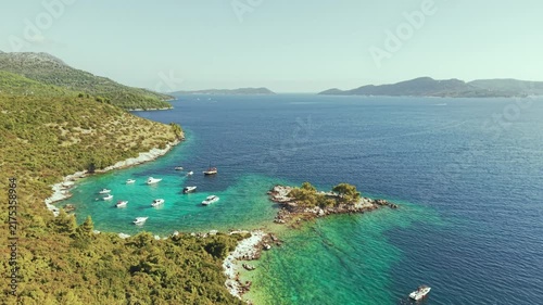 Aerial view of luxury yachts anchored in a turquoise bay surrounded by a rocky coastline and green forest. Summer seaside vacation scene. Drone view of the yachts.