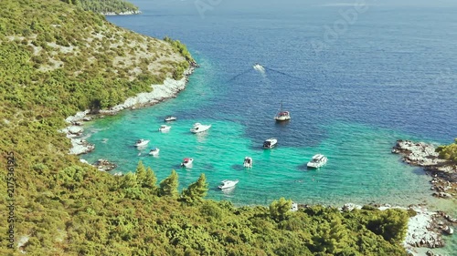 Aerial view of luxury yachts anchored in a turquoise bay surrounded by a rocky coastline and green forest. Summer seaside vacation scene. Drone view of the yachts.
