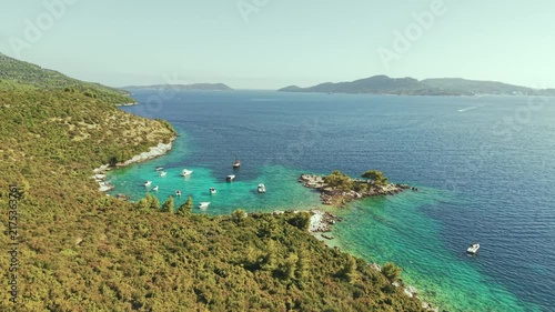 Aerial view of luxury yachts anchored in a turquoise bay surrounded by a rocky coastline and green forest. Summer seaside vacation scene. Drone view of the yachts.