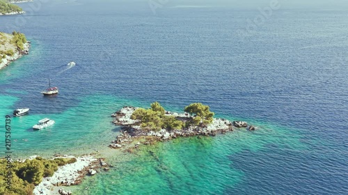 Aerial view of luxury yachts anchored in a turquoise bay surrounded by a rocky coastline and green forest. Summer seaside vacation scene. Drone view of the yachts.