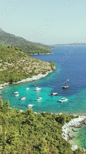 Aerial view of luxury yachts anchored in a turquoise bay surrounded by a rocky coastline and green forest. Summer seaside vacation scene. Drone view of the yachts.