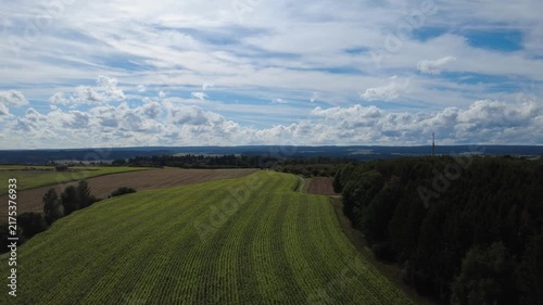Aerial view of green agricultural fields, open farmland and forest edges under a cloudy sky, showing a peaceful rural landscape with natural patterns and wide countryside scenery.