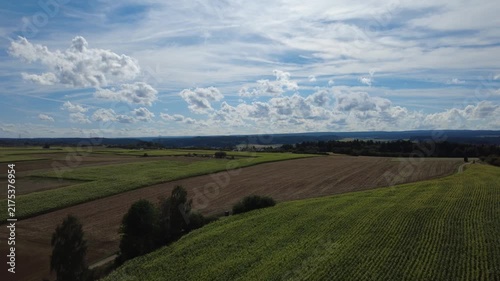 Aerial view of green agricultural fields, open farmland and forest edges under a cloudy sky, showing a peaceful rural landscape with natural patterns and wide countryside scenery.