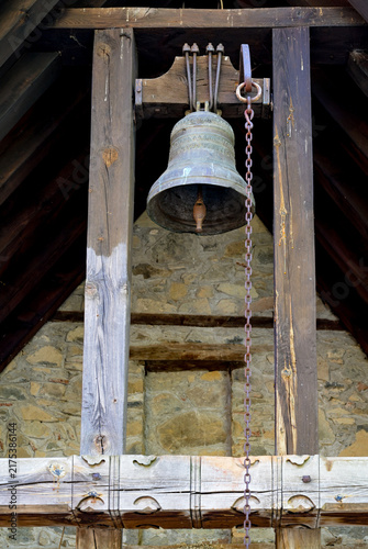 Old bronze bell hanging in a rustic wooden structure against a stone wall