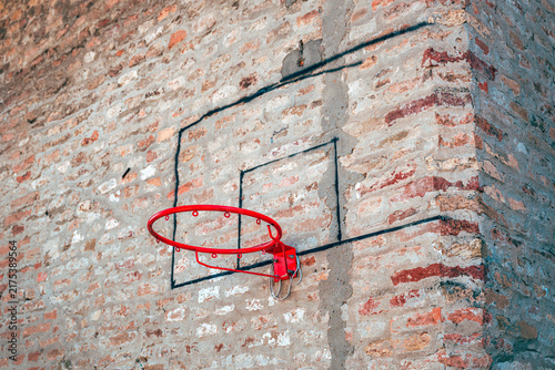 Фотография Red metal basketball rim mounted on an old weathered brick wall with painted backboard outlines