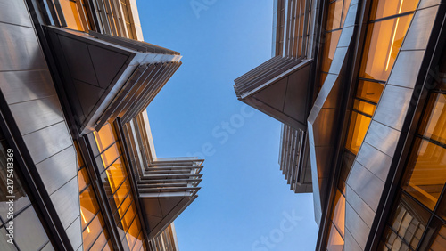 Modern architectural buildings featuring sharp geometric lines, reflective glass panels, and warm orange.