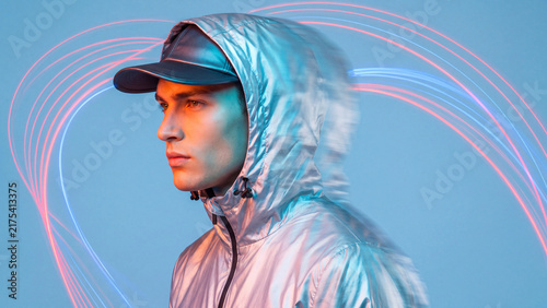 Man wearing a glossy silver jacket stands against a soft blue background with curved light trails.