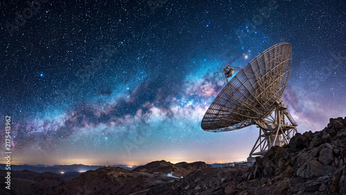Giant radio telescope dish pointing toward the breathtaking starry night sky of the milky way galaxy.