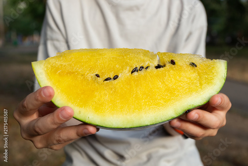 Photography A close-up of a yellow watermelon slice held by a boy outdoors in a park