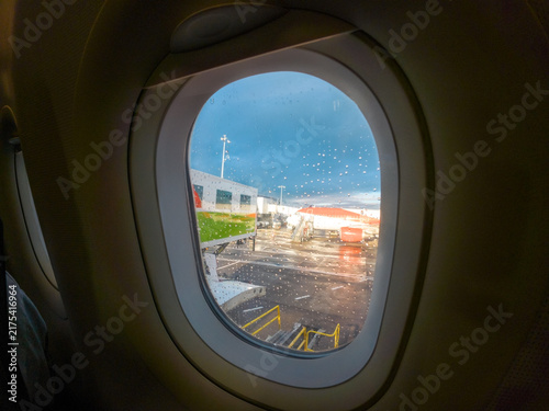Canvas Print A view looking out from an aircraft passenger window, capturing an airport apron during a wet, overcast day with visible raindrops on the glass