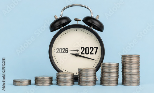 Alarm clock with stacked coins and 2026 to 2027 transition new year for symbolize financial planning, savings, investment growth, budgeting, retirement goals and wealth management.