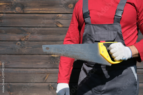 Cuadro en lienzo Skilled worker holding hand saw while wearing protective gloves and work overall