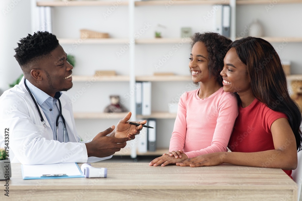 Fototapeta premium Smiling African American Doctor Engaging With Young Girl And Her Mother During Consultation At Clinic. Joyful Interaction Demonstrating Care, Support, And Professionalism In Healthcare Setting.