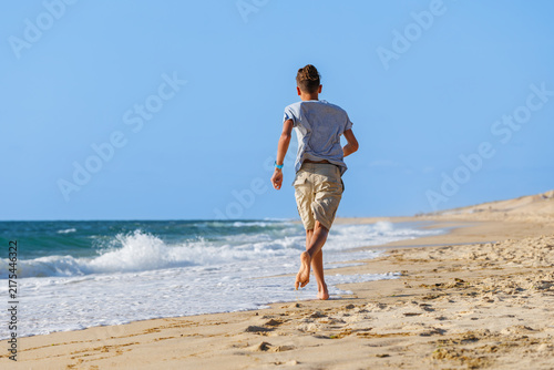 Teenager walking barefoot along sandy beach beside ocean waves