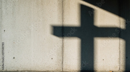 Sunlight casts a large cross shadow on rough concrete wall. Minimalist abstract concept of faith, hope, devotion and spirituality. Plenty of space for text.