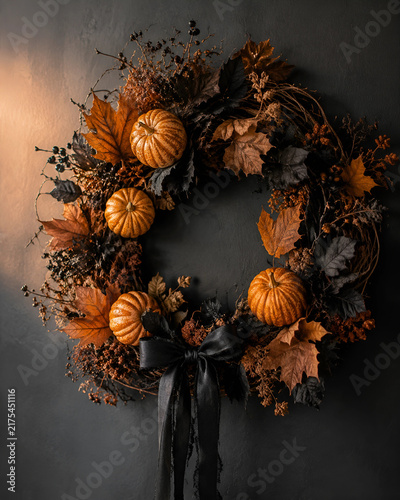A private home porch is decorated with pumpkins, black lanterns, a wreath and dry leaves. Gentle candlelight creates a cozy, refined Halloween atmosphere at dusk.