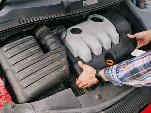 Mechanic hands removing the plastic protective cover from a car diesel engine inside a compact engine bay compartment.