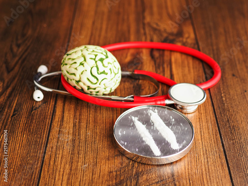 фотографія Stethoscope rests beside brain model and tow line of drugs on small mirror on wooden surface