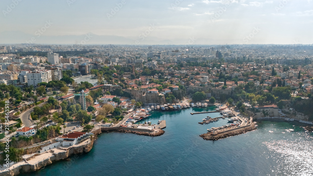 Obraz premium Aerial panorama of Antalya's Kaleici harbor with marina boats, historic old town rooftops, rocky coastline and sprawling cityscape in Turkey