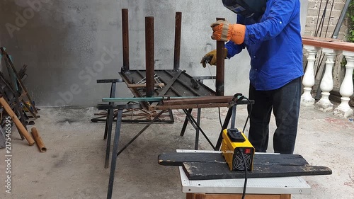 Welder holding last metal table leg in place for arc welding