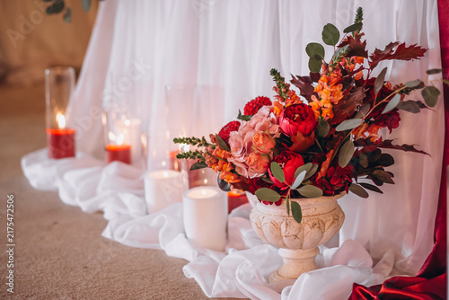 Foto Autumnal Elegance: A striking floral arrangement bursting with warm hues of red, orange, and deep green, complemented by flickering candlelight and draped fabric