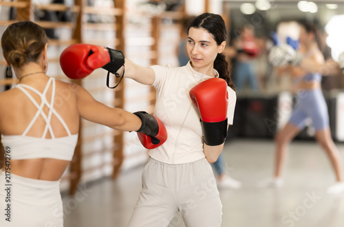 Фотография Sportive young girl training boxing in pair with his partner during sports class