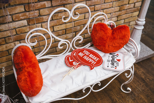 Konstfotografi Valentine's Day Photo Booth: A charming white bench with heart-shaped decorations holds a collection of romantic props, including plush hearts and a You Make Me Happy! sign