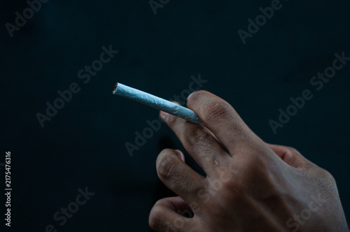 Принти на полотні Close-up of a hand holding an unlit cigarette against a dark background