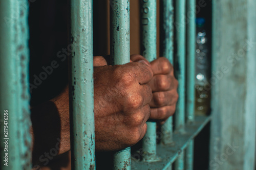 Fotografía Close up view of hands behind bars in a prison cell, symbolizing incarceration and the criminal justice system