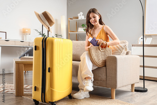 Travel preparation and vacation planning, young woman packing passport and boarding pass into straw bag with yellow suitcase in modern living room
