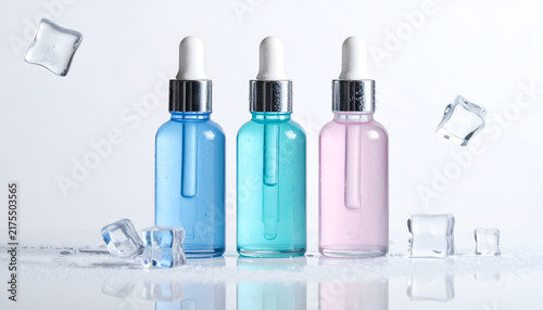 Three colorful serum bottles with droppers surrounded by ice cubes, set against a pristine white background