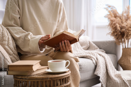 Young woman sitting on sofa and reading book at home, closeup