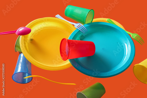 Fotografía Colorful plastic tableware levitating on red background